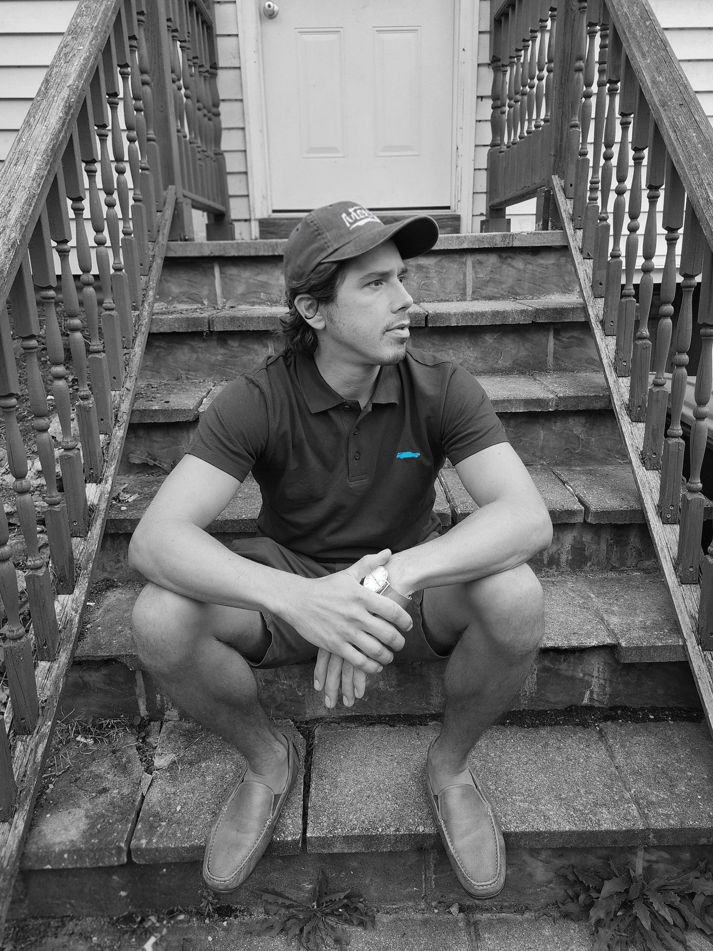 Person sitting on a set of stairs wearing a cap and polo shirt.