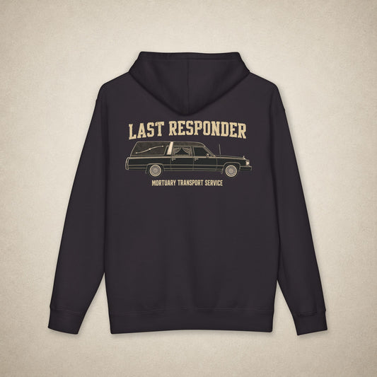 A dark navy blue hoodie shown from the back, featuring a vintage-style graphic of a hearse with the text 'LAST RESPONDER' and 'MORTUARY TRANSPORT SERVICE' in a beige color, set against a textured light beige background.
