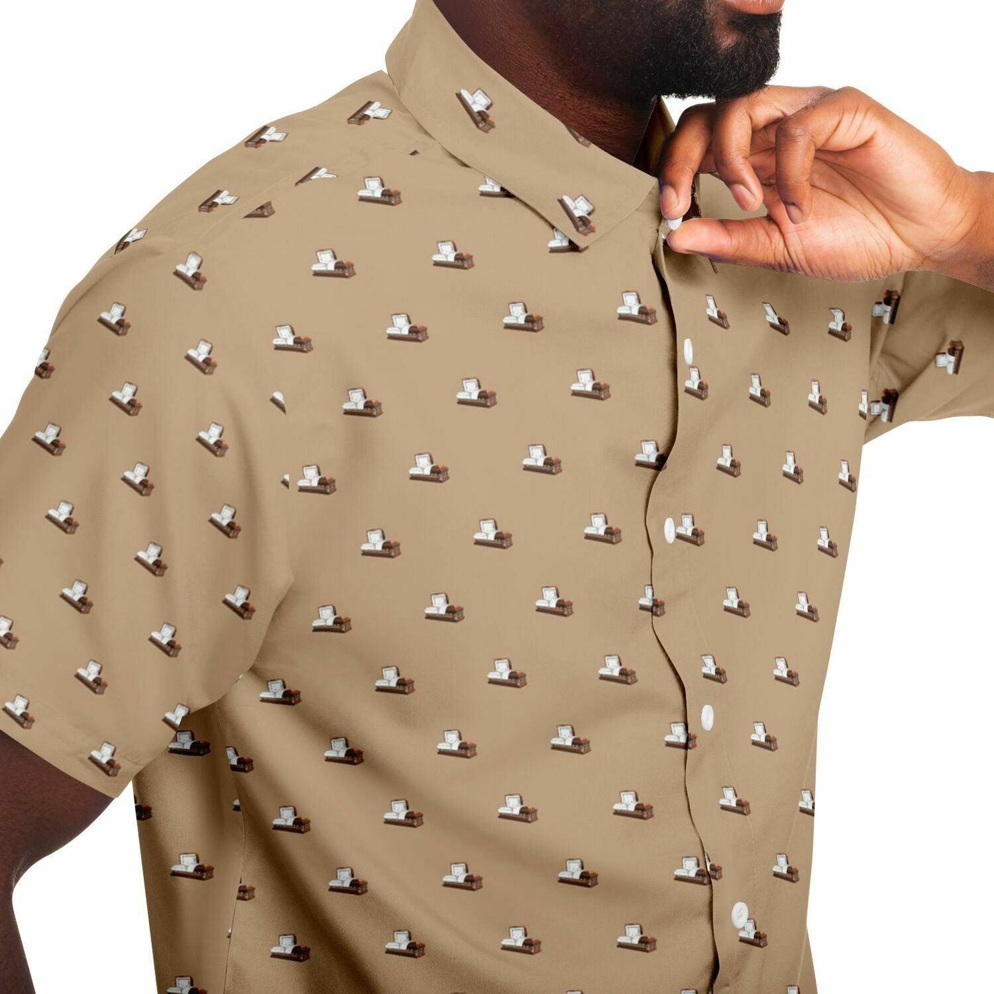 Close up view of a Man wearing a light brown button up shirt with short sleeves. The button down tee has a pattern on it containing dark brown metal coffins or caskets