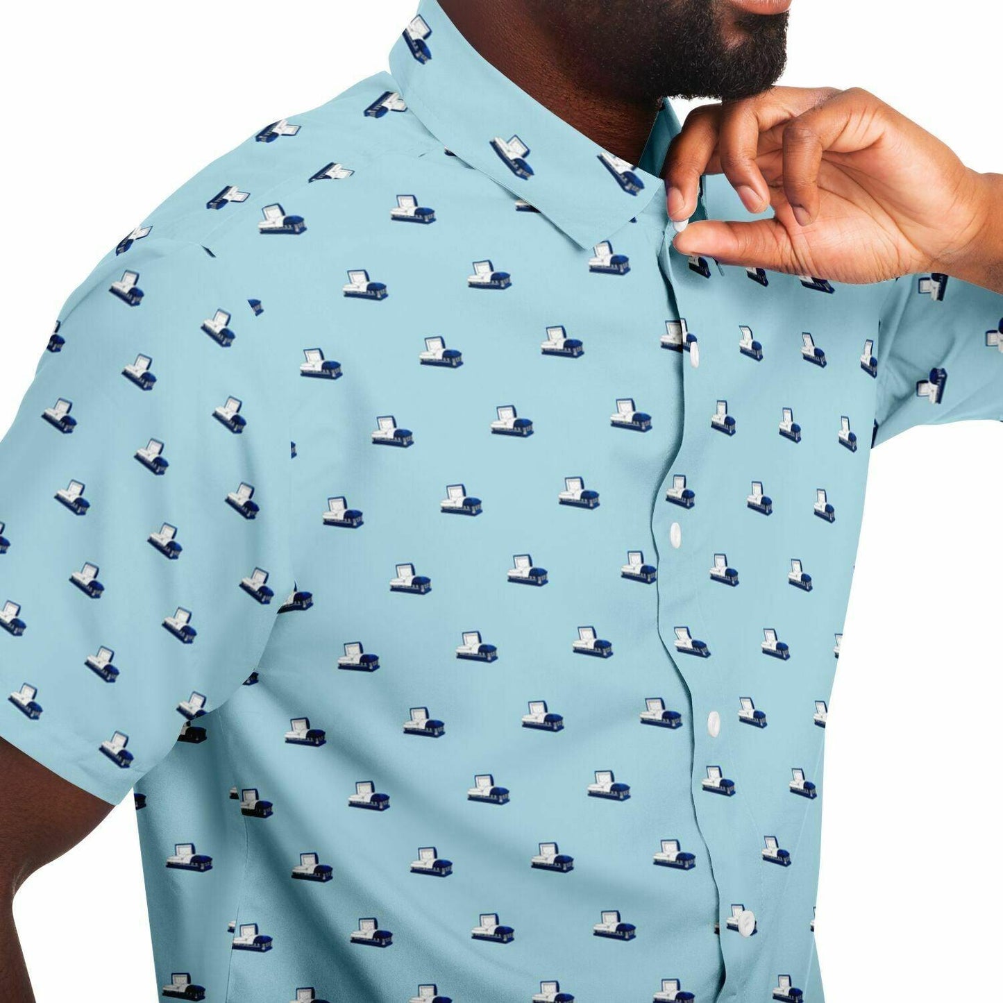 Model wearing a lighter blue button up shirt with short sleeves featuring a dark blue coffin pattern. Steel  metal open casket. Close up side angle view